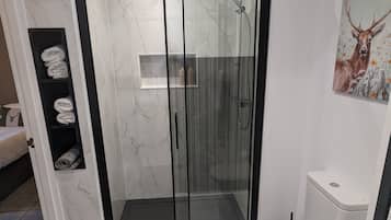 Un baño moderno con ducha envuelta en vidrio, inodoro y un perchero con toallas dobladas cuidadosamente.