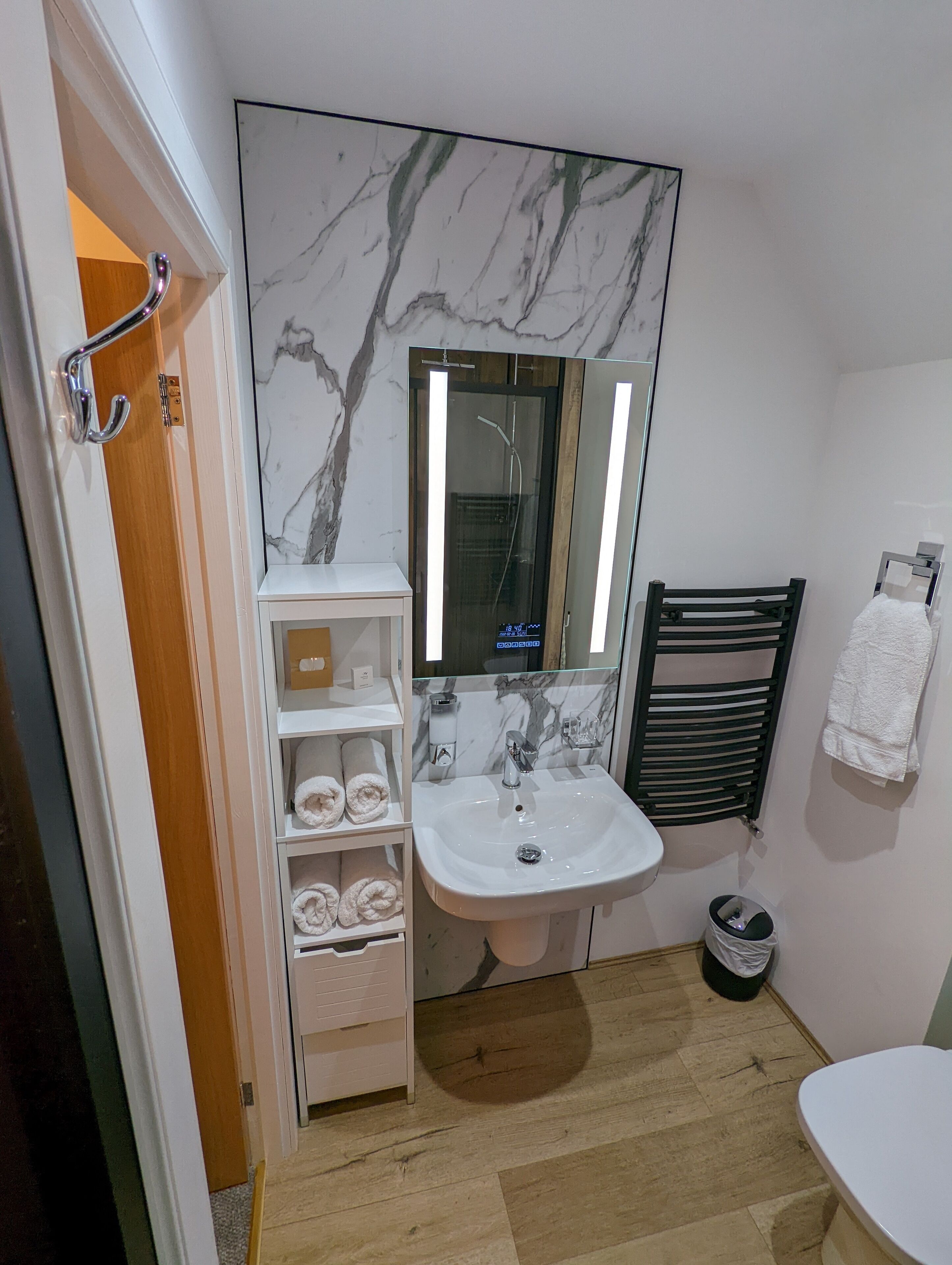 A bathroom with a marble backsplash, a white sink, a towel rack, and a wooden door.
