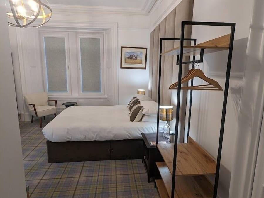 A hotel room with a bed, a chair, a desk, a hanging wardrobe, and a window.