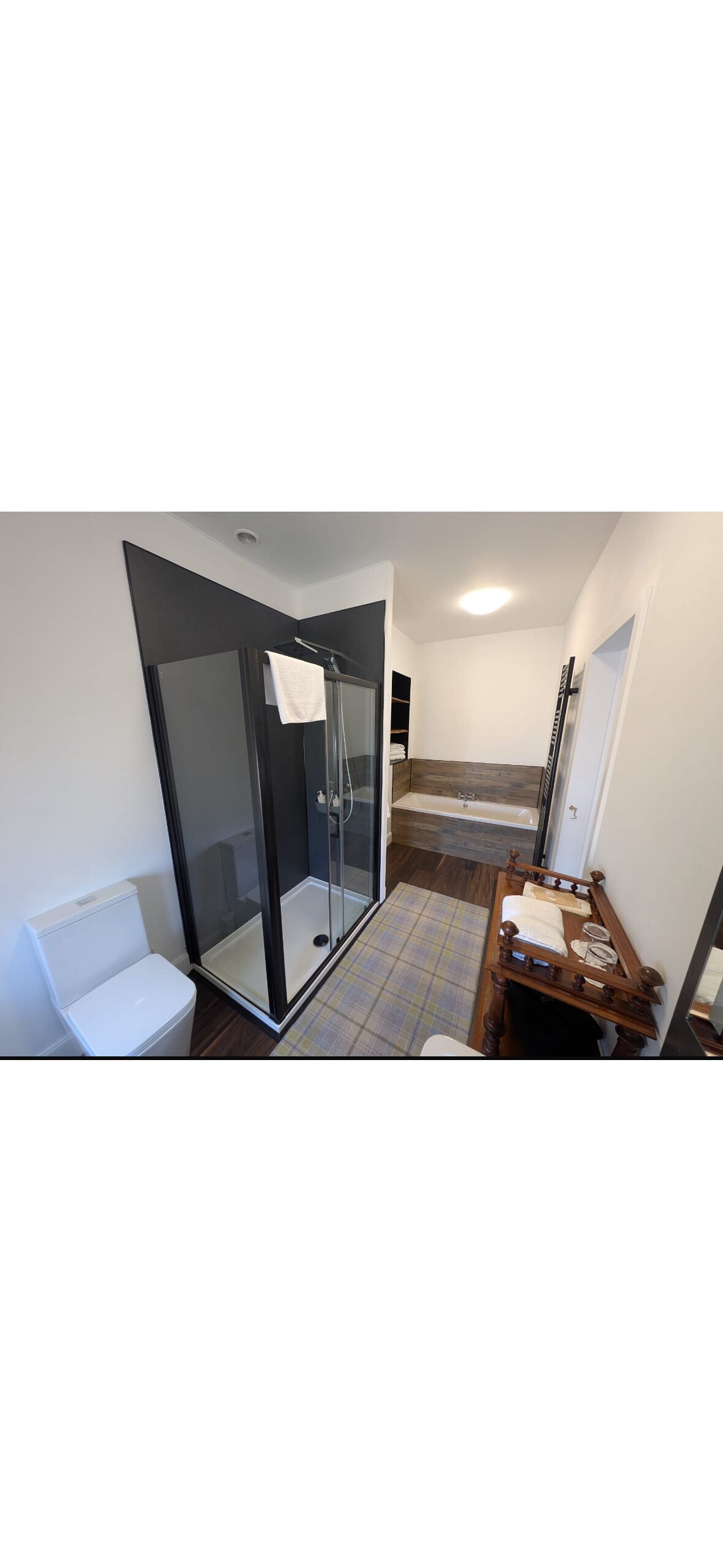 Un bany amb una cabina de dutxa de vidre, un vàter blanc i un tocador de fusta amb un mirall.