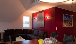 Un salon chaleureux avec un canapé aux couleurs sombres, une petite table sur laquelle se trouve une tasse jaune et un tableau représentant une scène de plage.