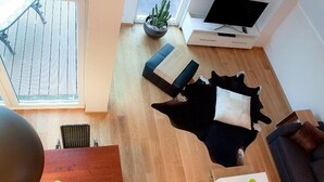 Un salon moderne avec un plancher en bois, un canapé noir, un meuble TV blanc et une plante en pot.