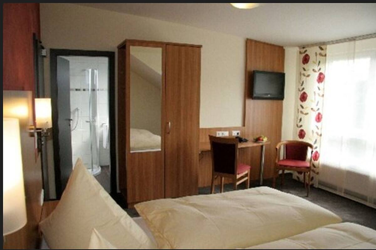 A hotel room with a bed, a desk, a chair, a TV, and a shower area.