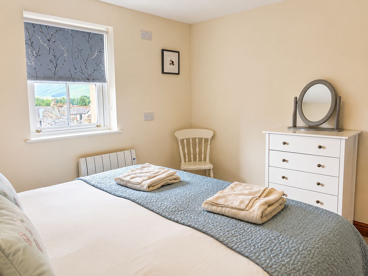 A bedroom with a bed, a dresser, a chair, and a window with a view.