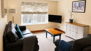 A living room with a sofa, a wooden coffee table, a TV, a cabinet, and a window with a view. - Howgills Apartment 9 (self-catering accommodation with free parking and Wi-Fi) (Sedbergh)