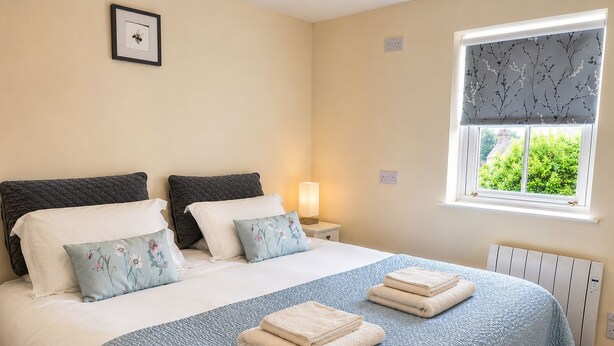 A double bed with a quilted blue bedspread, two pillows with floral designs, and two folded towels. - Howgills Apartment 9 (self-catering accommodation with free parking and Wi-Fi) (Sedbergh)
