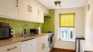 A modern kitchen with white cabinets, a dishwasher, a microwave, a toaster, and a window with a yellow blind. - Howgills Apartment 10 (self-catering accommodation with free parking and Wi-Fi) (Sedbergh)
