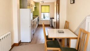 A compact kitchen with a refrigerator, stove, and sink. There is a dining table with chairs and a window with blinds. - Howgills Apartment 10 (self-catering accommodation with free parking and Wi-Fi) (Sedbergh)