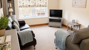 A living room with a sofa, a TV stand, a bookshelf, and a window with patterned curtains. - Howgills Apartment 11 (self-catering accommodation with free parking and Wi-Fi) (Sedbergh)