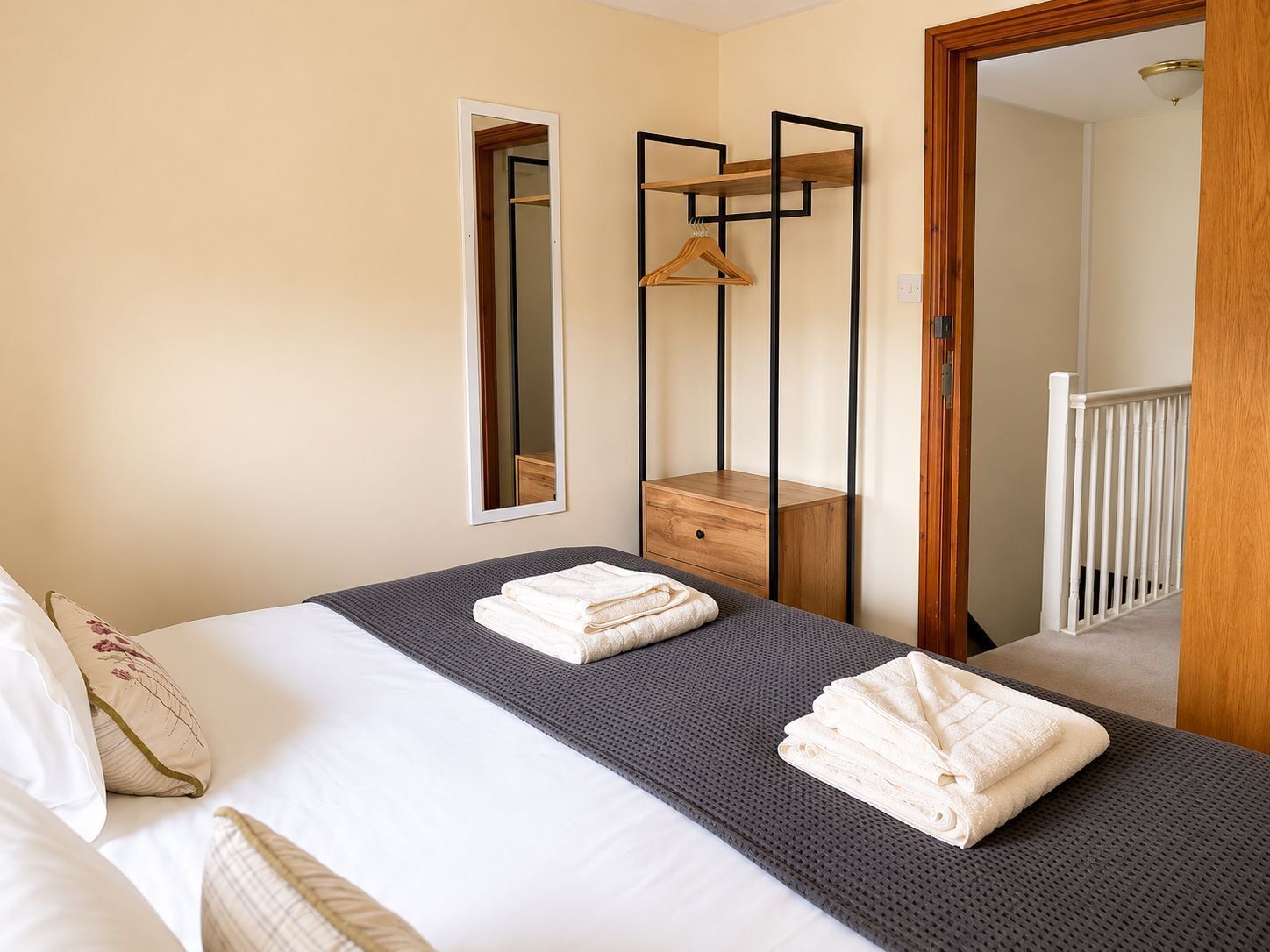 Een hotelkamer met een bed, nachtkastje, spiegel en een houten garderobe.