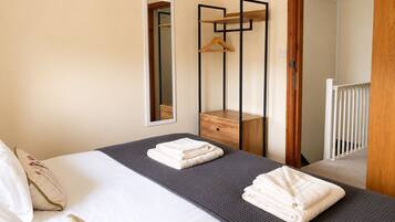 Een hotelkamer met een bed, nachtkastje, spiegel en een houten garderobe.