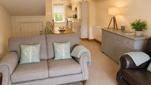 A living room with a sofa, a dark armchair, a dining table, and a kitchen in the background. - Howgills Apartment 11 (self-catering accommodation with free parking and Wi-Fi) (Sedbergh)