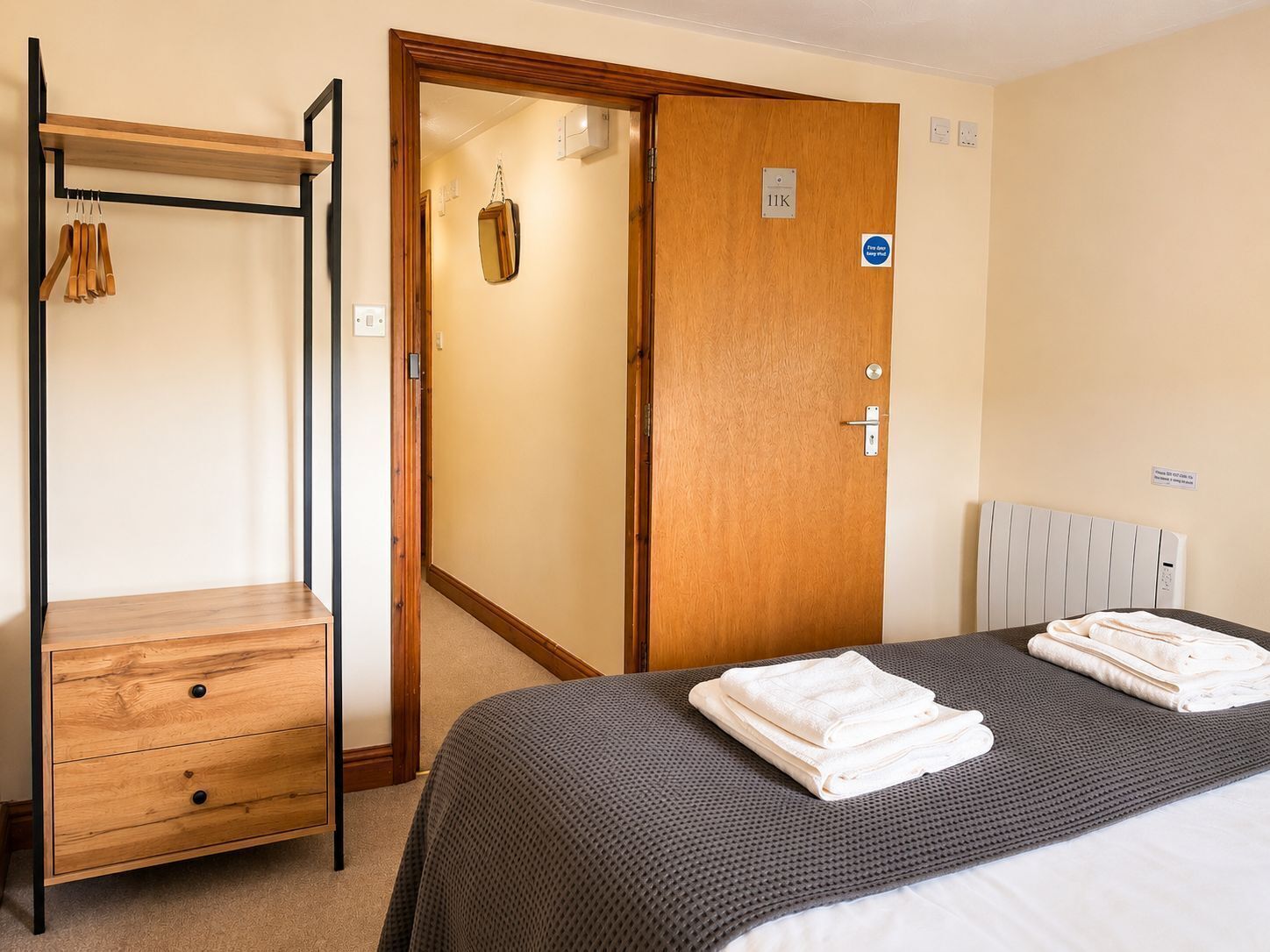 A hotel room with a bed, a wooden wardrobe, a door with a sign, and a radiator.