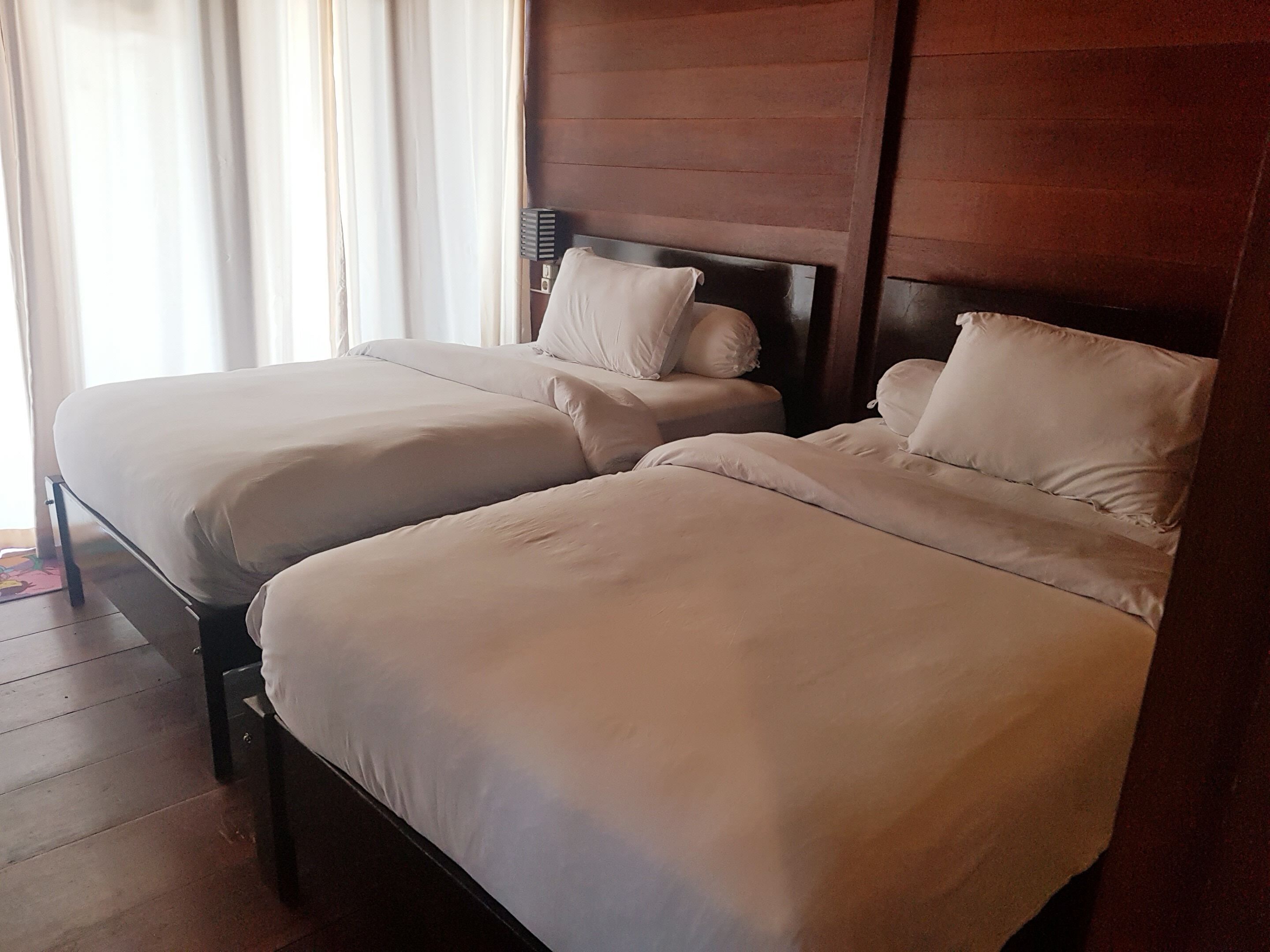 A hotel room with two beds, wooden headboards, and a window with curtains.