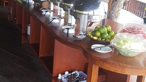 A buffet setup with various food items and utensils on wooden tables under a thatched roof. - Korpak Villa & Resort Raja Ampat (Waisai)