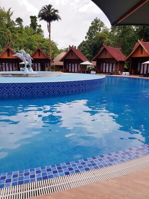 A swimming pool with a tiled edge, surrounded by wooden chalets with thatched roofs. - Korpak Villa & Resort Raja Ampat (Waisai)