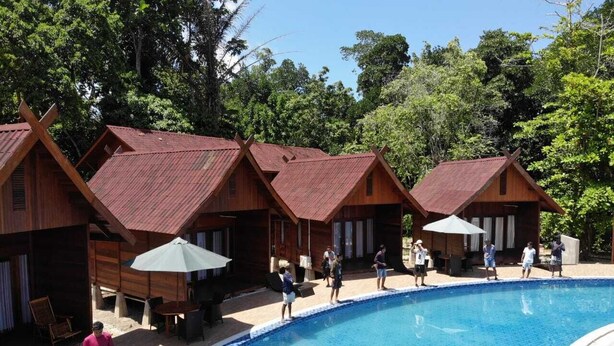 A pool area with wooden cabins, a swimming pool, and people around. - Korpak Villa & Resort Raja Ampat (Waisai)