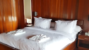 A large wooden bed with white linens and towels, a nightstand with a lamp, and a wooden floor. - Korpak Villa & Resort Raja Ampat (Waisai)