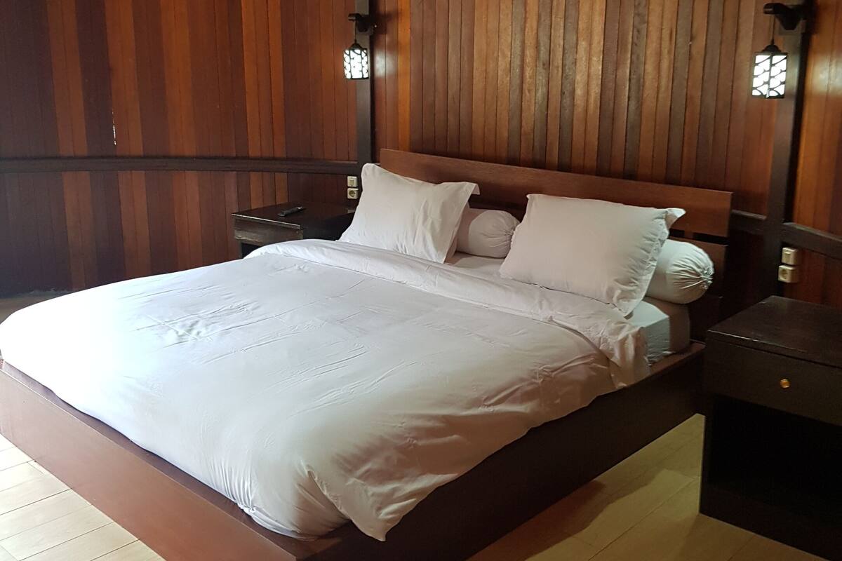 A wooden-paneled room with a bed, nightstands, and wall-mounted lights.