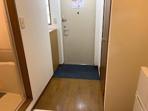 A narrow hallway with a wooden floor, a blue mat at the entrance, and a door with a sign above it.