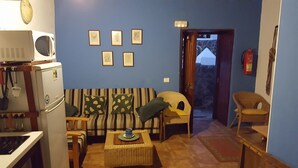 A living room with a striped sofa, a small table, a chair, and a microwave. There are framed pictures on the wall and a door leading to another room. - RURAL HOUSE FINCA PARAISO. for a fantastic stay north of Tenerife (San Cristóbal de La Laguna)