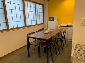 Een eethoek met een houten tafel en stoelen, een magnetron, en een kitchenette met een gele wand.