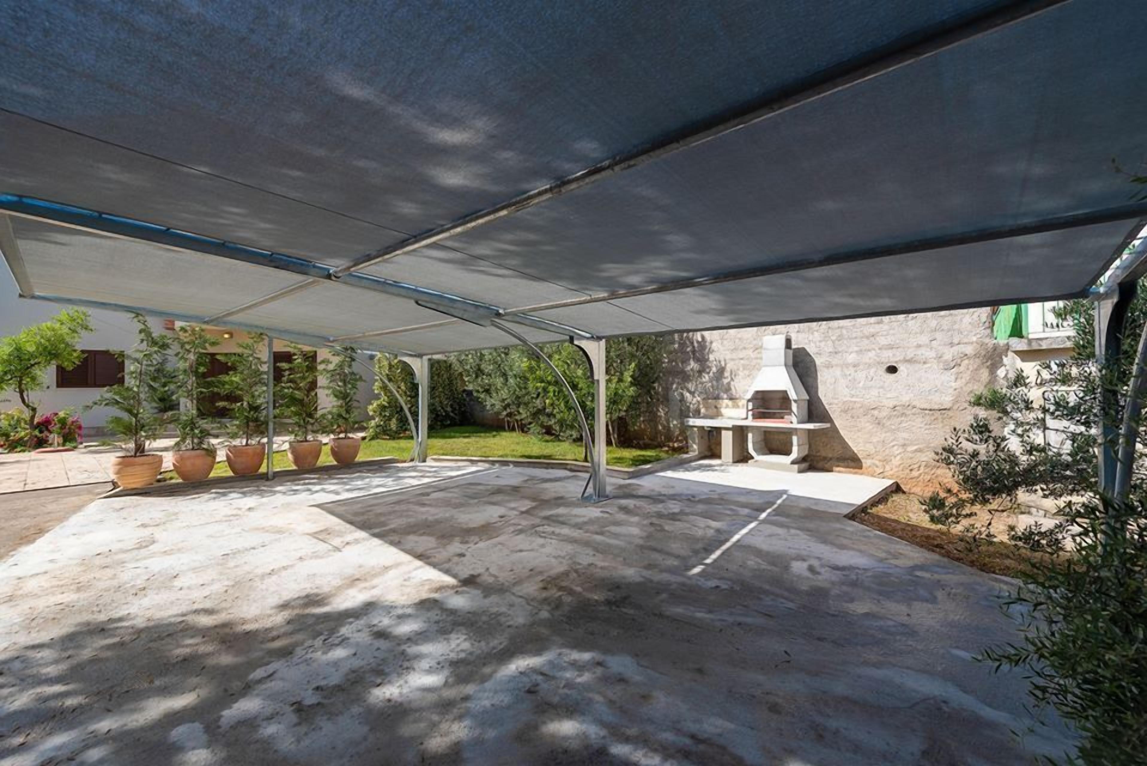 A covered outdoor patio area with a barbecue grill, potted plants, and a stone wall in the background.