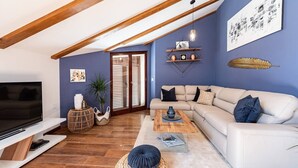 A modern living room with a white sofa, wooden beams, a TV, and a bookshelf. - Zen Luxury Apartments (Zadar)