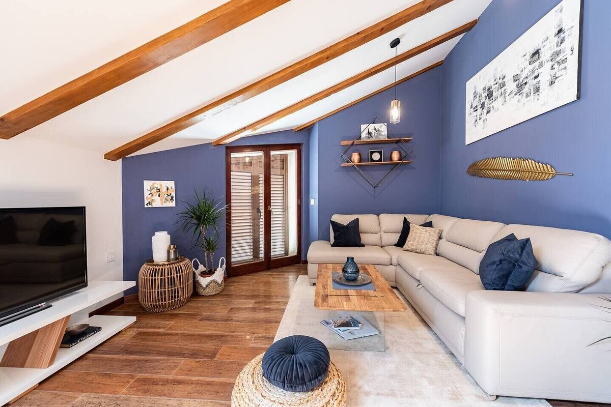 A modern living room with a white sofa, wooden beams, a TV, and a bookshelf.