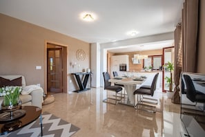 Een moderne woonkamer met een bank, een salontafel en een eethoek met een tafel en stoelen. Achtergrond is een keuken met een eettafel en stoelen.