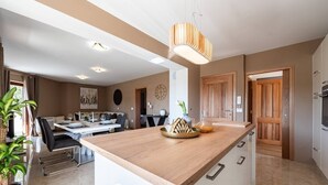A modern kitchen with a central island, wooden cabinets, and a dining area with a table and chairs. - Zen Luxury Apartments (Zadar)