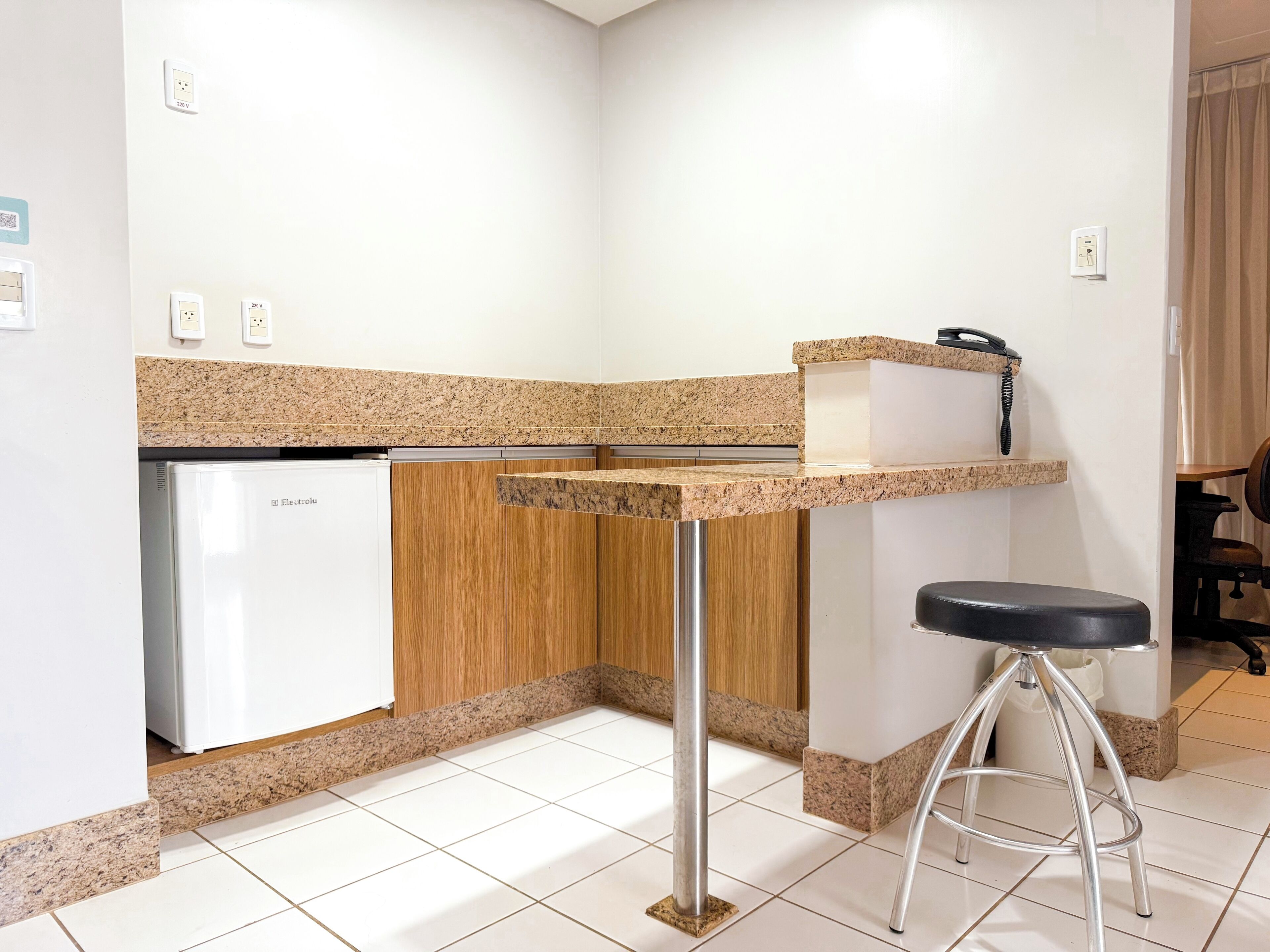 Une cuisine de taille réduite, dotée d’un plan de travail en granit, d’un lave-vaisselle blanc et d’un tabouret de bar.