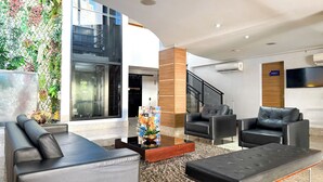 A modern lobby with black leather sofas, a coffee table, and a decorative plant wall. - STAY Sun Square (Goiania)