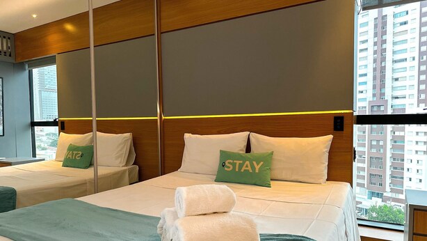 A hotel room with two beds, a green towel on the bed, and a pillow with the word "STAY". - STAY Sun Square (Goiania)