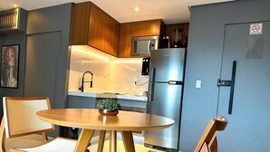 A modern kitchen with wooden cabinets, a stainless steel refrigerator, and a dining area with a round table and two chairs. - STAY Sun Square (Goiania)