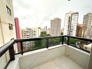 Un balcón con suelo de mármol y barandilla de cristal que ofrece vistas a un paisaje urbano con edificios altos.