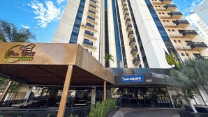A high-rise hotel with multiple balconies, a prominent 'Sun Square Suites Hotel' sign, and a 'Dow Will Garden' sign. - STAY Sun Square (Goiania)