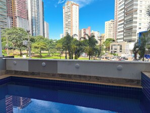 Vista desde un balcón con piscina, con vistas a un paisaje urbano con edificios altos y un parque con árboles.