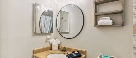 A bathroom with a sink, mirror, towel rack, and a small shelf with toiletries.