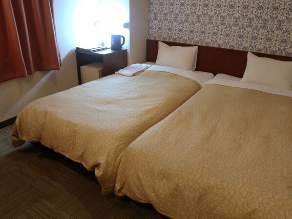 A hotel room with two beds, a nightstand with a coffee maker, and a patterned wallpaper on the wall.