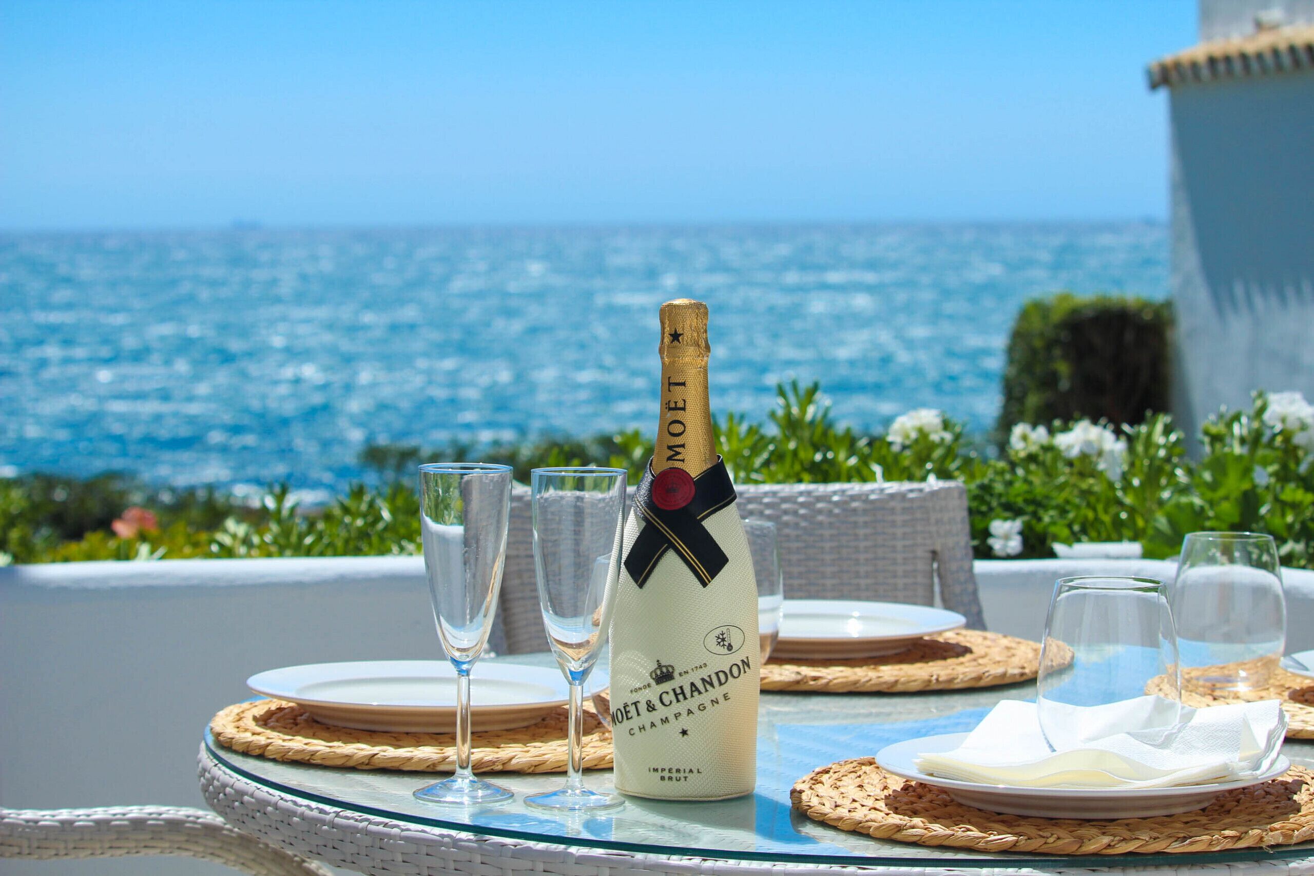 A bottle of Moët & Chandon champagne on a table with glasses and plates, overlooking the sea.