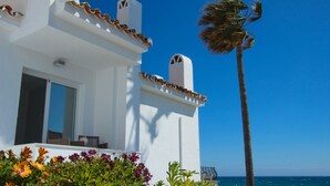 A white building with a balcony overlooking the sea, a palm tree, and colorful flowers in the foreground. - Rocas del Mar I - Front Line Beach (Mijas Costa)