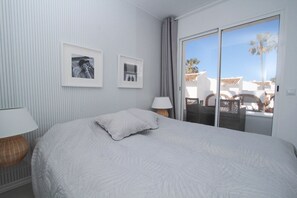 A hotel room with a large bed, two framed photographs on the wall, a lamp, and a view of palm trees through a sliding glass door. - Rocas del Mar I - Front Line Beach (Mijas Costa)