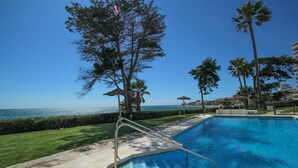 A swimming pool with a view of the ocean, surrounded by palm trees and a clear sky. - Rocas del Mar I - Front Line Beach (Mijas Costa)