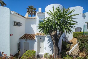 A white building with a tiled roof, a door, and a small garden area with a palm tree. - Rocas del Mar I - Front Line Beach (Mijas Costa)