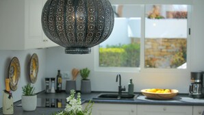 A modern kitchen with white cabinets, a black countertop, a decorative hanging light, and a window with a view of greenery. - Rocas del Mar I - Front Line Beach (Mijas Costa)