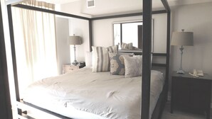 A four-poster bed with a neutral color scheme, a bedside table with a lamp, and a mirror on the wall. - Yacht Club S #1-1104 4 Bedroom Condo by RedAwning (North Myrtle Beach)