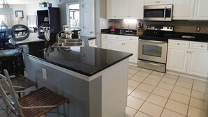A kitchen with white cabinets, a black countertop, stainless steel appliances, and a small island with a sink. - Yacht Club S #1-1104 4 Bedroom Condo by RedAwning (North Myrtle Beach)