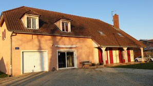 A two-story house with a gravel driveway, a garage, and a covered porch with red curtains. - Au Fil des Lacs (Précy-Saint-Martin)