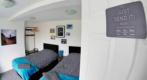 Een slaapkamer met twee bedden, een stapelbed, een wandrek en een deur met een bord waarop faciliteiten staan aangegeven, zoals fiets, park en lodge.